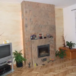 Wykończony salon z obudowanym kominkiem z płytek imitujących kamień, dekoracyjną ścianą, telewizorem i parkietem w jodełkę.